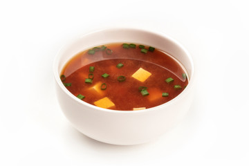 A photo of a bowl of miso soup with tofu and scallions on a white background with copy space