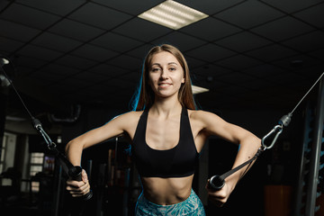 Active beautiful fitness model girl trains pectoral muscles on a simulator in the gym.