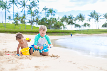Two cute boys playing in the sand together on a tropical beach vacation. Candid, Full length photo with lots of copy space on a idyllic, scenic beach.
