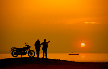 Fototapeta na wymiar Silhouette Couple with a motorbike at river side at sunset.