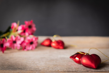 Red plastic hearts placed on a wooden table There is a flower placed on the left back There are red plastic hearts placed backside.