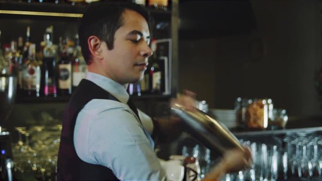 Asian bartender shaking cocktail with ice inside shaker on bar counter backround
