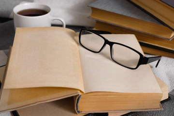 Stack of open vintage books with glasses and  cup of tea