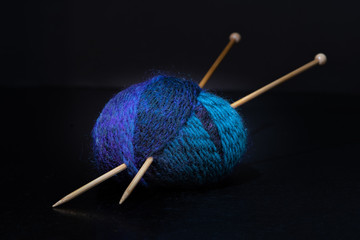 ball of yarn and wooden knitting needles on a black background