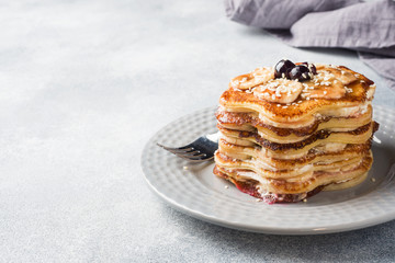 Pancake cake with bananas and berry syrup, selective focus, grey background.