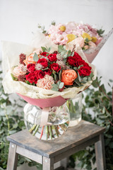 two beautiful fresh cut bouquet of mixed flowers in vase on wooden table. The work of the florist at a flower shop. Red spray roses and other flowers