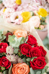 two beautiful fresh cut bouquet of mixed flowers in vase on wooden table. The work of the florist at a flower shop. Red spray roses and other flowers