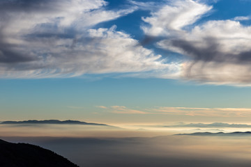 Obraz premium Valley filled by fog with blue sky with clouds and warm sunset colors