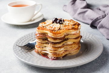 Pancake cake with bananas and berry syrup, selective focus, grey background.