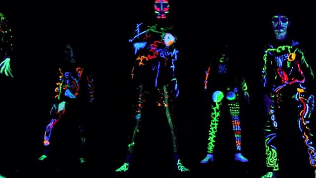 creative group of children in colorful costumes that glow in the dark, creates abstract movements. The costumes that glow in the dark room are painted in paints