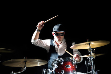 Professional drummer playing on drum set on stage on the black background