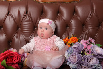 Fototapeta na wymiar girl five months in a pink dress with bouquets of flowers