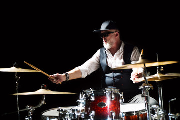 Professional drummer playing on drum set on stage on the black background