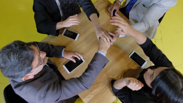 Indian mixed friends in a cafe, top shot looking down, as they hip hip hurray with hands and punch the air to celebrate their victory and success of their business plan and project 