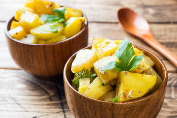 Baked potatoes with spices and herbs in wooden plate.