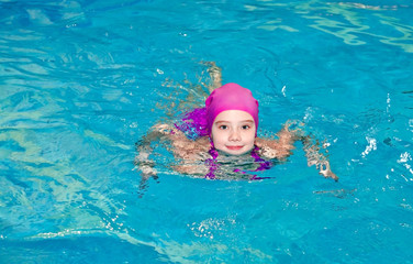 Portrait of cute smiling little girl child swimmer in pink swimming suit and cap in the swimming poo