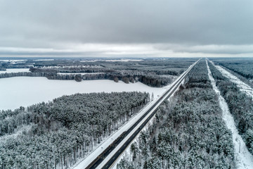 Freeway passing through the winter forest. The road goes away to the horizon line.