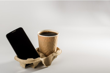 smartphone and a glass of coffee on cardboard tray on gray background. concept of business Breakfast