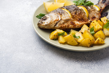 Baked fish carp with lemon greens and potatoes on a plate. Copy space