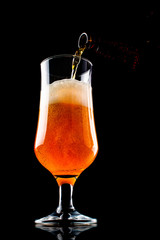 Beer is pouring into a glass from bottle on black background