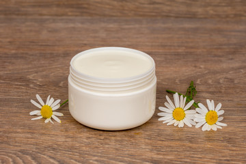 Obraz na płótnie Canvas body cream opened plastic jar with chamomile flowers on wooden table