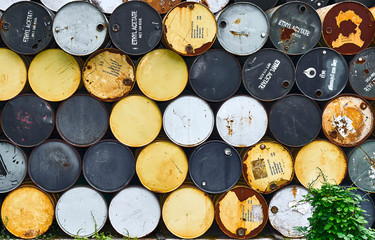 Many old, rusty drums, partially with 'Ethyl Acetate' signage on it, piled up orderly in many rows....