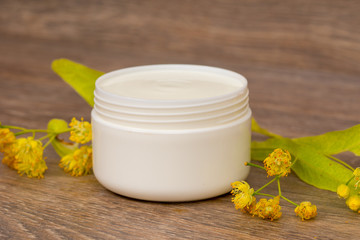 Obraz na płótnie Canvas body cream opened plastic jar with chamomile and linden flowers on wooden table