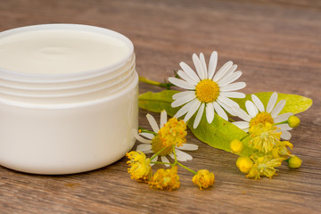 Fototapeta na wymiar body cream opened plastic jar with chamomile and linden flowers on wooden table