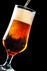 Beer is pouring into a glass from bottle on black background