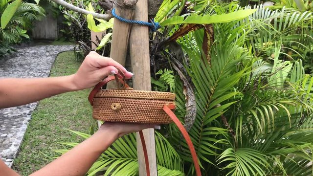 Woman hands with stylich eco friendly rattan bag on a tropical background. Bali island.