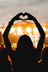 Girl with heart-shape symbol enjoying her favorite group on the concert.