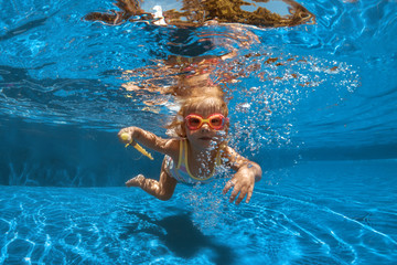Pretty little girl swimming in swimming pool.