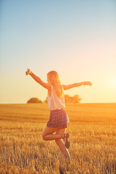 Cute young woman jumping in a wheat field.