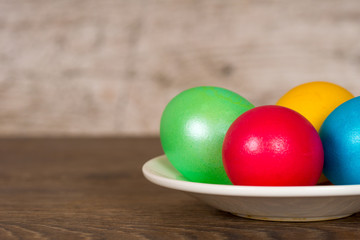 Obraz na płótnie Canvas red, yellow, green and blue easter eggs in plate on wooden table