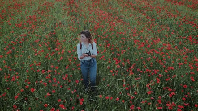 Beautiful young milennial fashion blogger or creative freelance photographer, creates content for social media. Influencer with vintage camera in field of poppy flowers, romantic and dreamy