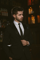 Attractive man wearing black tuxedo in whiskey bar.