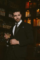 Attractive man wearing black tuxedo in whiskey bar.