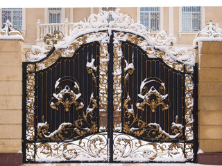 Beautiful forged gates covered in snow. Artistic forging. Close-up. Black gates decorated with gold...