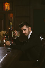 Attractive man wearing black tuxedo in whiskey bar.
