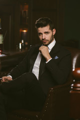 Attractive man wearing black tuxedo in whiskey bar.