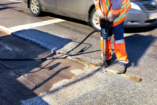 A worker clears a piece of asphalt with a pneumatic jackhammer in road construction.