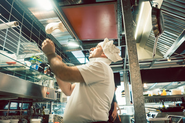 Low-angle side view of an experienced cook tossing dough while preparing pizza in the kitchen of a...