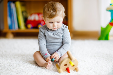 Adorable baby girl playing with educational toys . Happy healthy child having fun with colorful different wooden toy at home. Early development for children with nature toy.