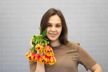 Beautiful girl in the brown dress with flowers tulips in hands on a light background	