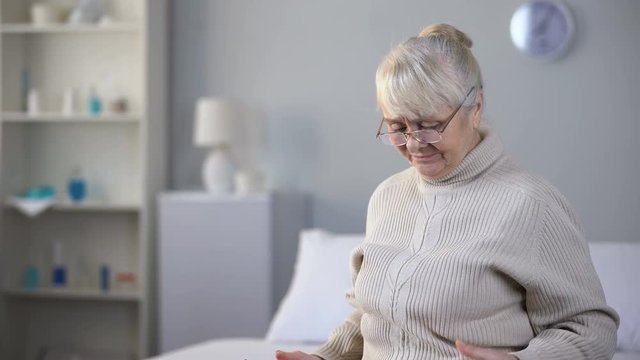 Sad aged woman wearing eyeglasses and watching photo album, missing family