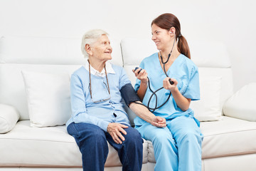 Pflegerin beim Blutdruck messen bei einer Seniorin