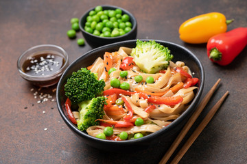 Asian udon noodle stir fry with broccoli, green pea, carrot and pepper in bowl. Tasty oriental...
