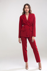 young elegant woman in red trouser suit standing in the studio on gray background