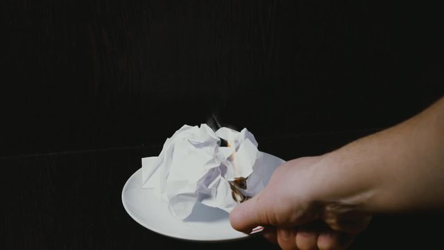 women's hands set fire to a crumpled sheet of paper on a plate