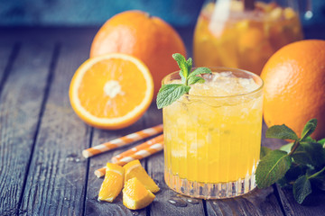 Glass jar of fresh orange juice with ice and fresh fruits on dark table.